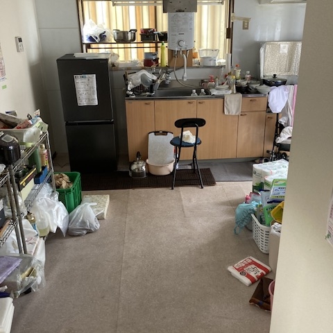 栃木県壬生町の戸建て住宅・片付け前のキッチン。床に不用品が広がり、調理スペースが確保できない状態。