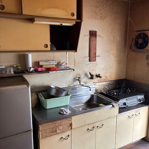 宇都宮市の市営住宅キッチンの片付け前の様子。シンクや収納棚に汚れが目立ち、換気扇周りも油汚れが付着している状態。