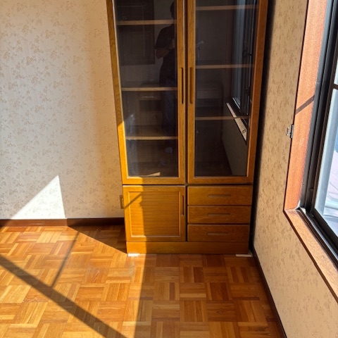 ガラス扉付きキャビネットを残して片付けが完了した部屋の様子。陽の光が差し込む清潔な空間に整理された状態。