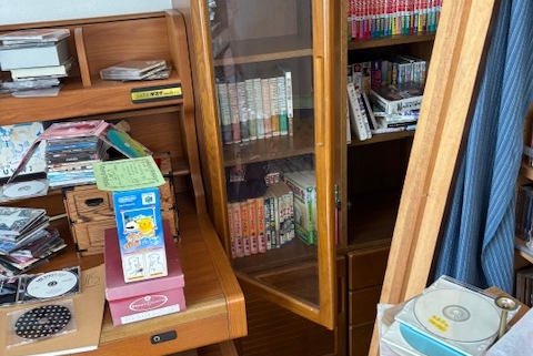 宇都宮市の解体予定住宅・2階洋室の片付け前の様子。書棚や机の上に本やCD、雑貨が多く残されている。