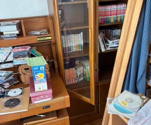 宇都宮市の解体予定住宅・2階洋室の片付け前の様子。書棚や机の上に本やCD、雑貨が多く残されている。