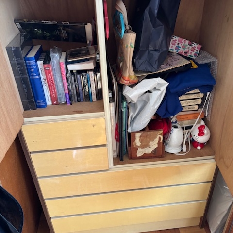 タンスの中に衣類や雑貨、本などが残された状態の収納スペース。解体前の整理作業前の様子。