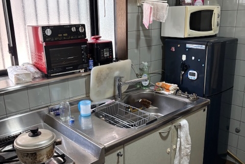 片付け前の和室の様子。押し入れに日用品が残り、畳の上にも生活用品が置かれている状態。