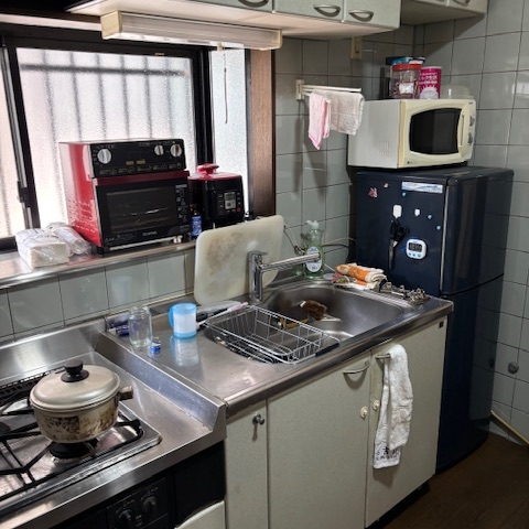 片付け前の和室の様子。押し入れに日用品が残り、畳の上にも生活用品が置かれている状態。