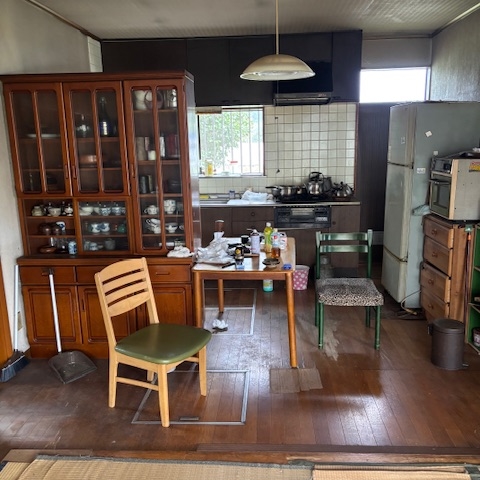 売却前のキッチンとダイニングの様子。天井に汚れがあり、シンク周りや床に生活用品が残っている状態。