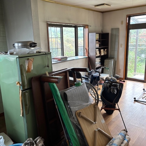 片付け前のリビング。床に汚れがあり、奥のキッチンには家電や家具が残されたままの状態。